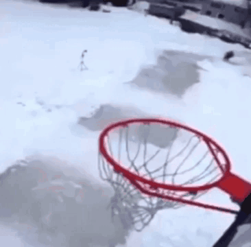 A Person Is Playing Basketball In The Snow With A Basketball Hoop In The Background . GIF