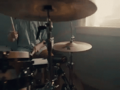 A Person Is Playing Drums In Front Of A Window In A Room . GIF