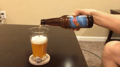 A Person Is Pouring A Bottle Of Beer Into A Glass On A Coaster GIF