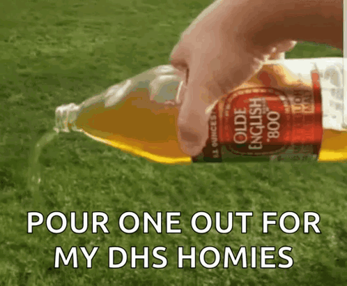 A Person Is Pouring A Bottle Of Olde English Apple Cider Into A Grassy Field . GIF