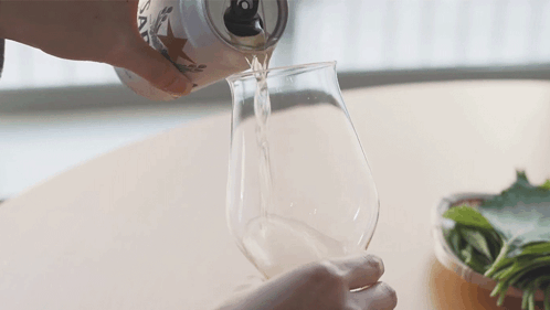 A Person Is Pouring A Can Of Beer Into A Glass GIF
