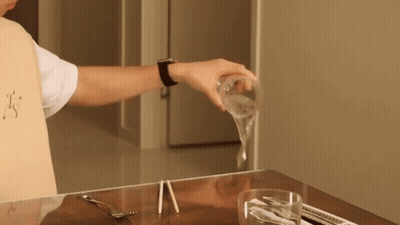 A Person Is Pouring A Glass Of Water On A Table With Chopsticks GIF