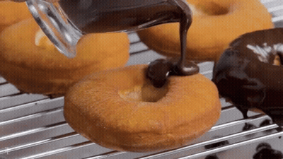 A Person Is Pouring Chocolate On A Donut On A Cooling Rack GIF