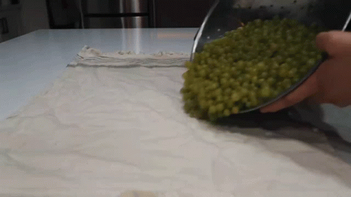 A Person Is Pouring Green Peas Into A Bowl On A Cloth GIF