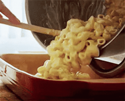A Person Is Pouring Macaroni And Cheese Into A Casserole Dish With A Spatula . GIF