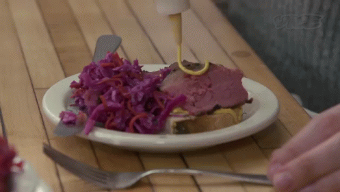 A Person Is Pouring Mustard On A Plate Of Food On A Wooden Table . GIF