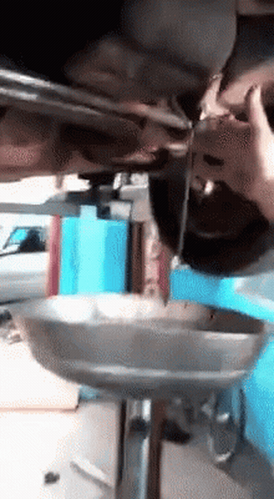 A Person Is Pouring Oil Into A Metal Tray Under A Car GIF