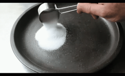 A Person Is Pouring Sugar Into A Pan With A Measuring Cup GIF