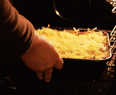 A Person Is Putting A Casserole Dish In The Oven GIF