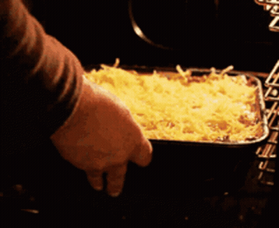 A Person Is Putting A Casserole Dish In The Oven GIF