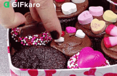A Person Is Putting A Heart On A Cupcake In A Box Filled With Cupcakes . GIF