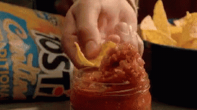 A Person Is Putting A Tortilla Chip Into A Jar Of Salsa . GIF