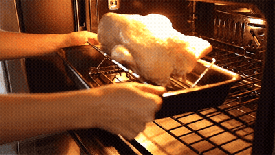 A Person Is Putting A Turkey In An Oven GIF