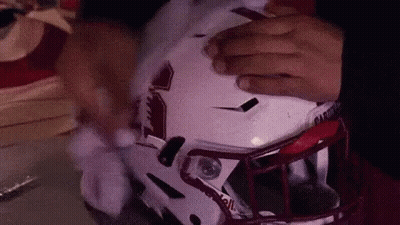 A Person Is Putting On A Football Helmet With Their Hands . GIF