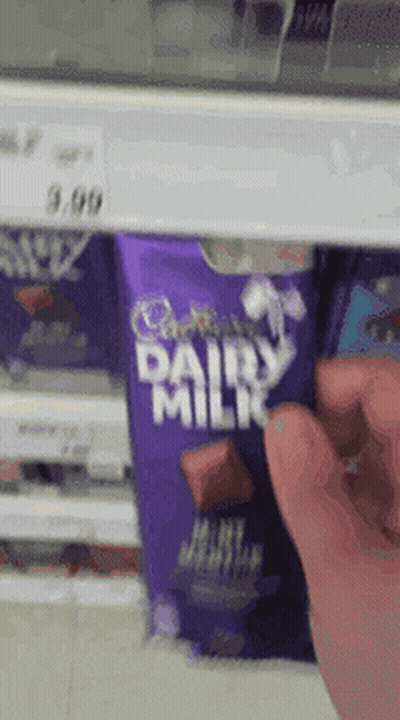 A Person Is Reaching For A Cadbury Dairy Milk Bar In A Store GIF