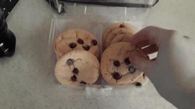 A Person Is Reaching For A Chocolate Chip Cookie From A Plastic Container GIF