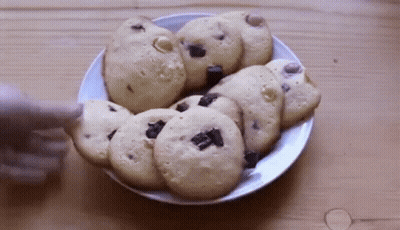 A Person Is Reaching For A Cookie On A Plate Of Cookies GIF