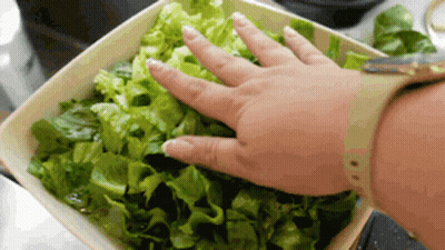 A Person Is Reaching Into A Bowl Of Lettuce With Their Hand GIF