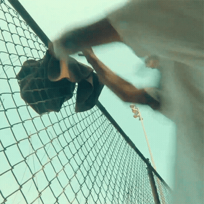 A Person Is Reaching Over A Chain Link Fence GIF