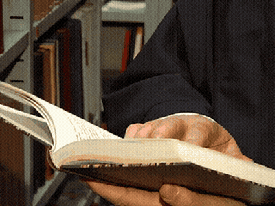 A Person Is Reading A Book In Front Of A Shelf GIF