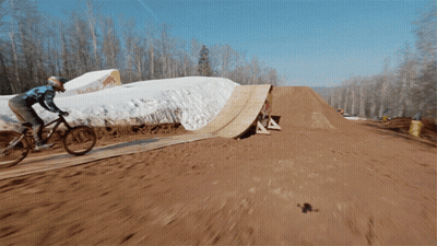 A Person Is Riding A Bike On A Dirt Track With A Red Bull Sign In The Background GIF