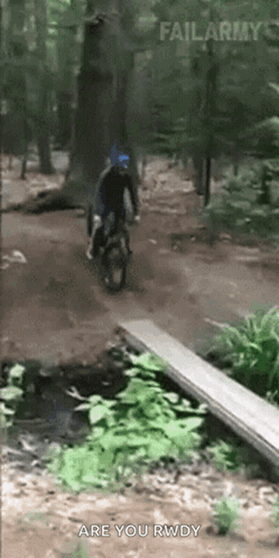 A Person Is Riding A Bike Over A Wooden Bridge In The Woods GIF