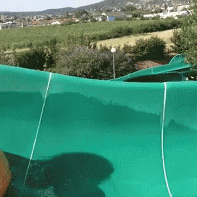 A Person Is Riding A Green Water Slide In A Park GIF