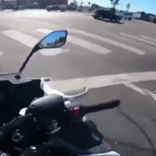 A Person Is Riding A Motorcycle Down A Street And Looking At The Rear View Mirror . GIF