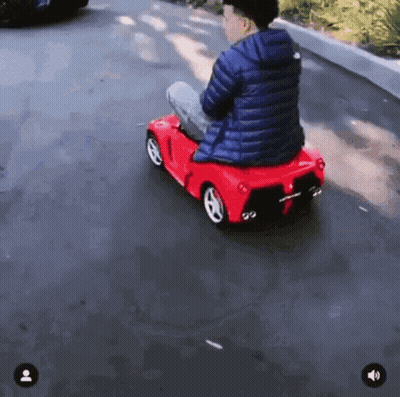 A Person Is Riding A Red Toy Car Down A Road GIF