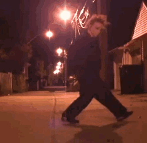 A Person Is Riding A Skateboard Down A Sidewalk At Night . GIF