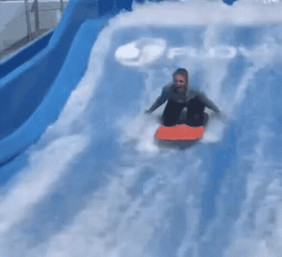 A Person Is Riding A Surfboard Down A Water Slide In The Water . GIF