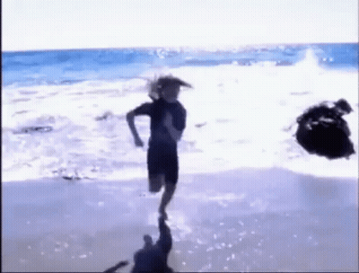 A Person Is Running On A Beach With A Rock In The Background . GIF
