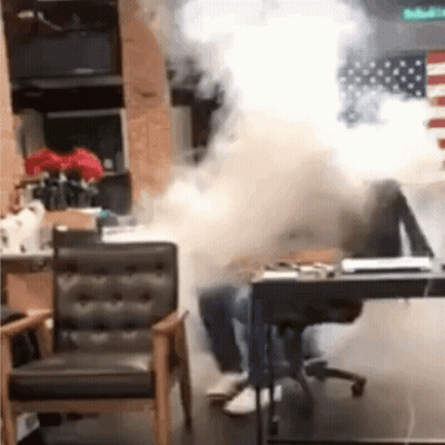 A Person Is Sitting At A Desk In A Room With Smoke Coming Out Of The Window . GIF