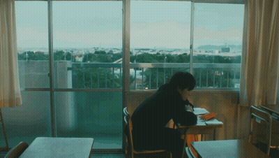 A Person Is Sitting At A Desk In Front Of A Window GIF