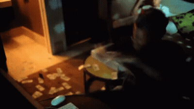 A Person Is Sitting At A Table With Cards On The Floor In A Dark Room GIF