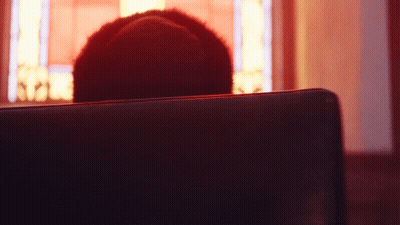 A Person Is Sitting In A Dark Room With A Red Light Behind Them GIF