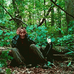A Person Is Sitting In The Woods With Their Hands On Their Head GIF