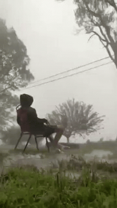 A Person Is Sitting On A Chair In The Grass In A Field . GIF