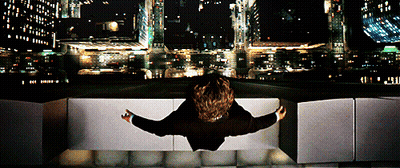 A Person Is Sitting On A Ledge Looking Out Over A City At Night GIF