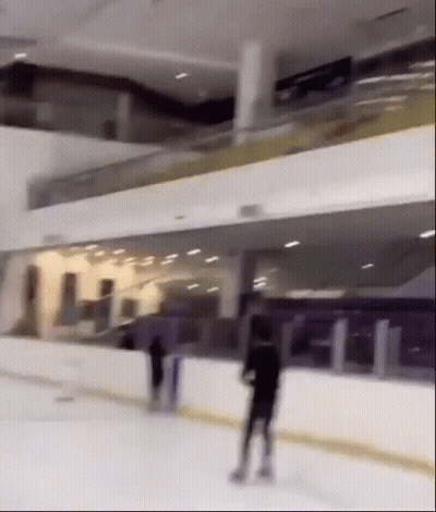 A Person Is Skating On An Ice Rink In A Large Building GIF