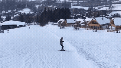 A Person Is Skiing Down A Snow Covered Slope With Houses In The Background GIF