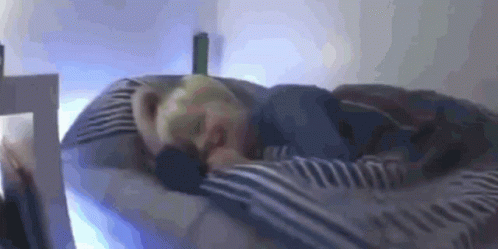 A Person Is Sleeping On A Bed With A Striped Blanket . GIF
