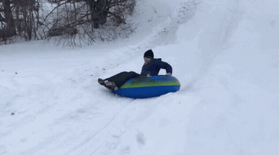 A Person Is Sliding Down A Snowy Hill On A Blue And Green Tube GIF