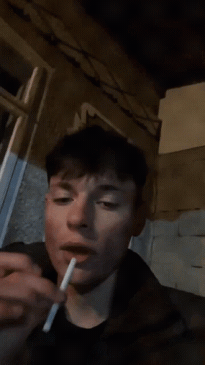A Person Is Smoking A Cigarette In Front Of A Wall With A Floral Design On It GIF