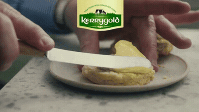 A Person Is Spreading Butter On A Biscuit With A Label For Kerrygold In The Background GIF