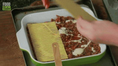 A Person Is Spreading Cheese On Top Of A Casserole Dish With Food Tube Written On The Bottom . GIF