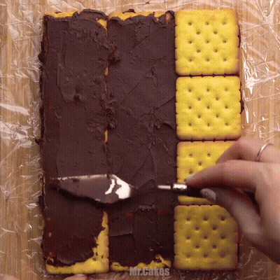 A Person Is Spreading Chocolate Icing On Crackers With The Words Mr.cakes Visible GIF