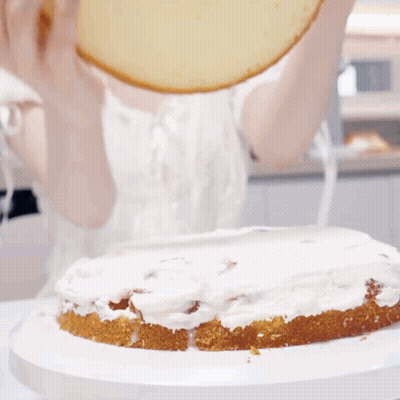 A Person Is Spreading Frosting On A Cake On A Plate GIF