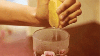 A Person Is Squeezing Lemon Juice Into A Glass . GIF