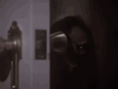 A Person Is Standing In A Dark Room Holding A Door Handle . GIF